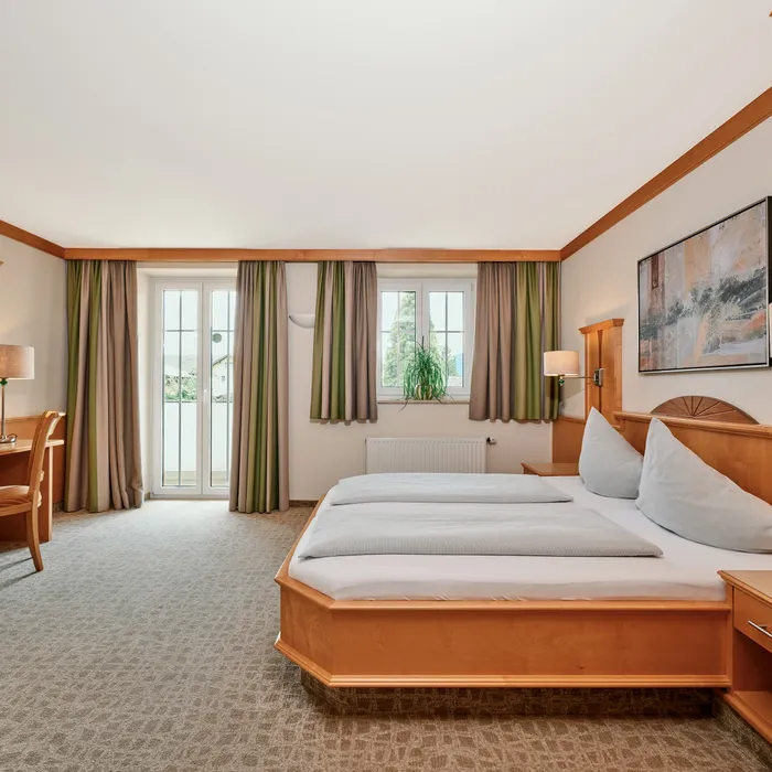 Geräumiges Hotelzimmer mit Doppelbett, Holzmöbeln, Schreibtisch und Tageslicht vom Balkon